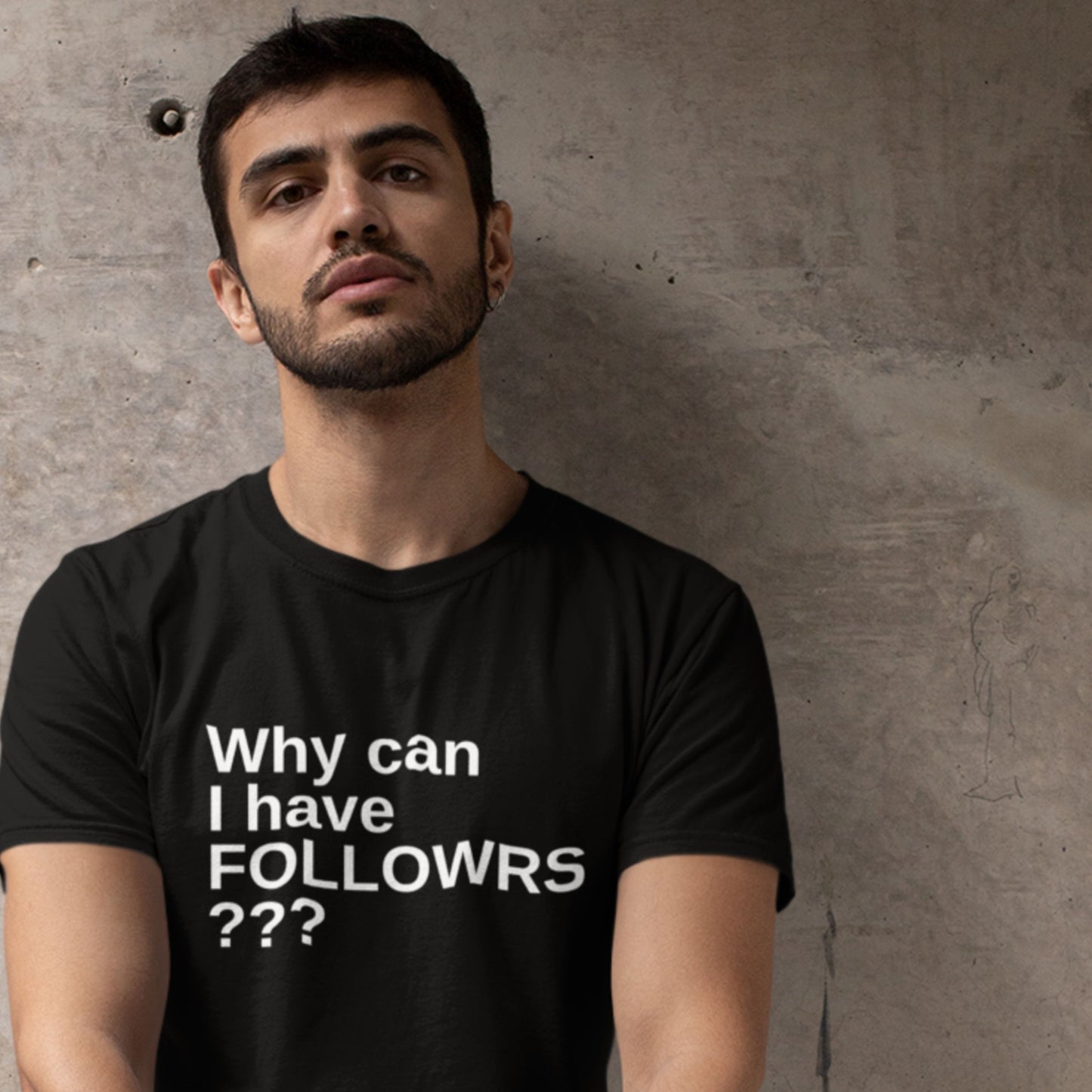 Man wearing a black t-shirt with text against a concrete wall.