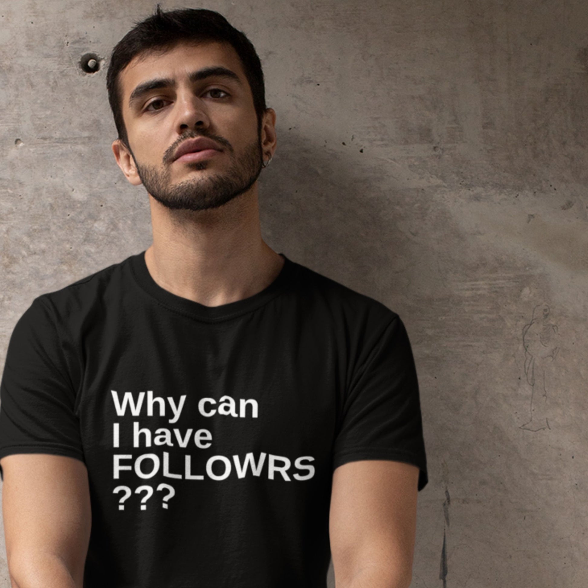 Man wearing a black t-shirt with text against a concrete wall.