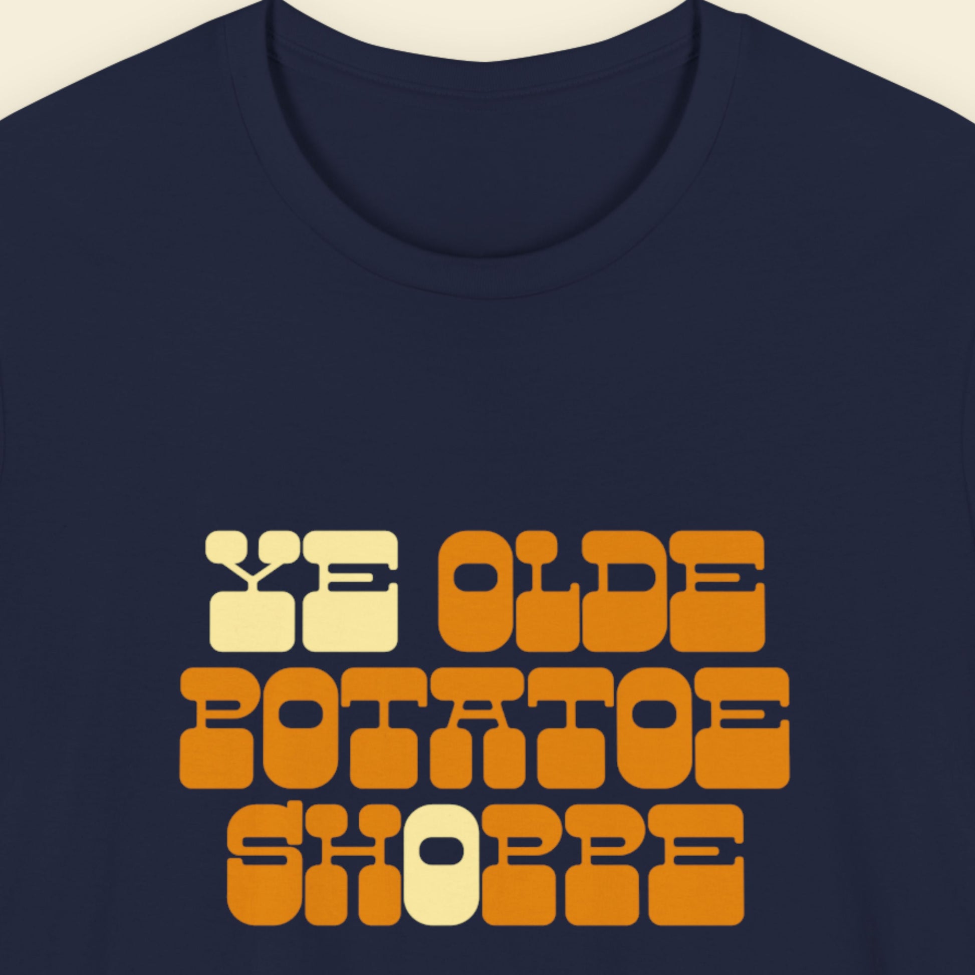 Navy blue t-shirt with 'YE OLDE POTATOE SHOPPE' text in orange and beige on a beige background.