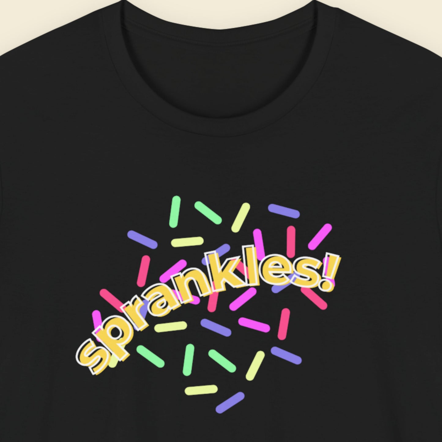 Black t-shirt with colorful 'sprankles!' text design on a beige background.