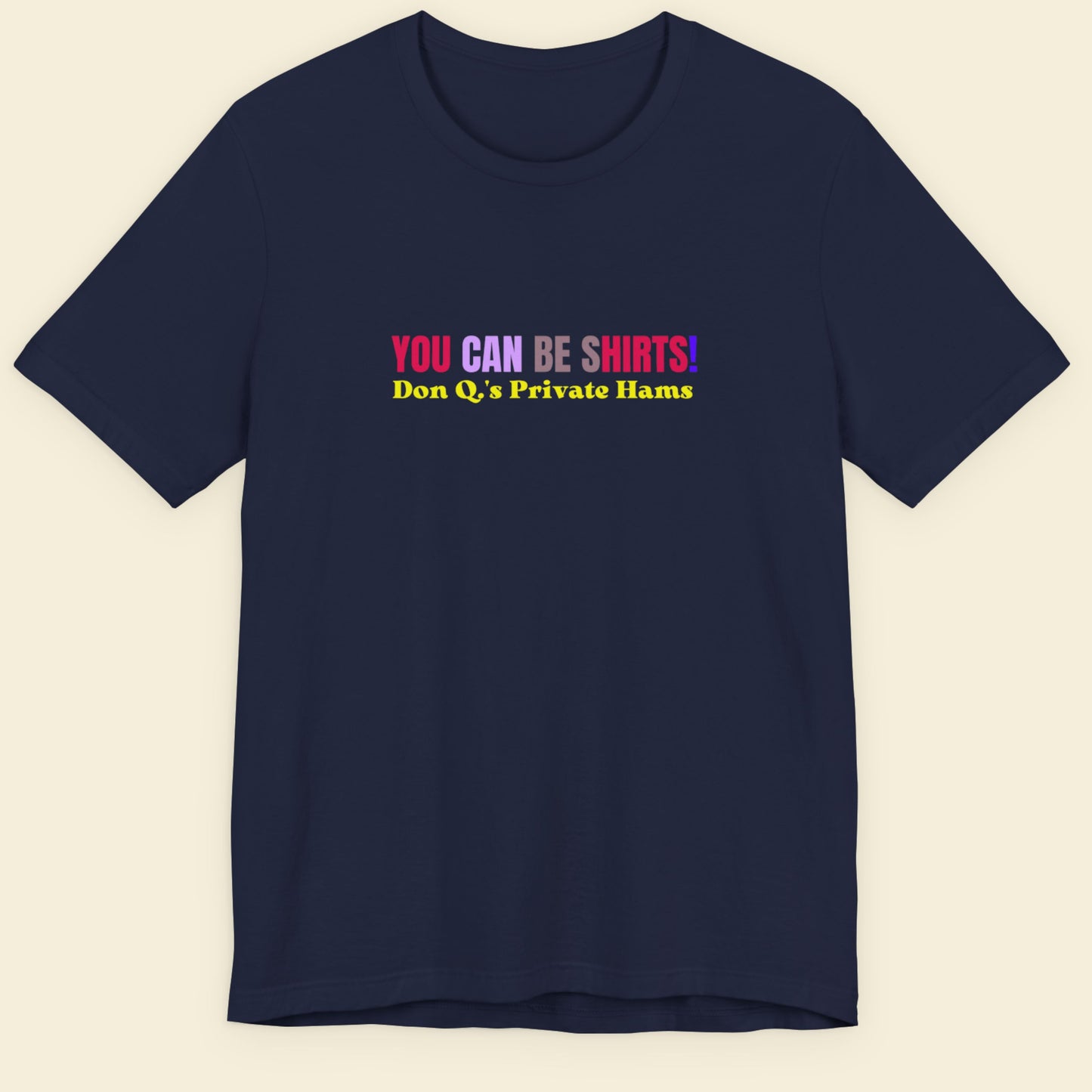Navy blue t-shirt with multicolored 'you can be shirts!' text on a beige background.