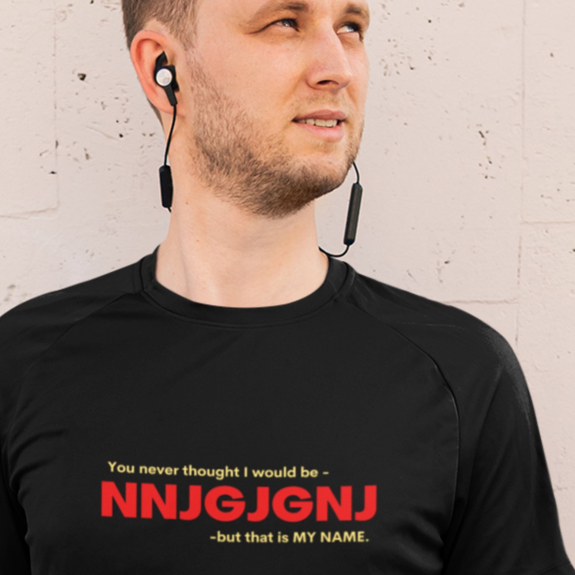 Man wearing a black t-shirt with red and yellow text against a beige brick wall.