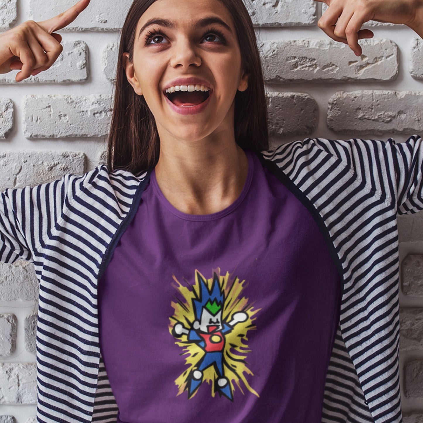 Happy woman wearing a t-shirt with a fun, colorful cartoon illustration in front of a brick wall.