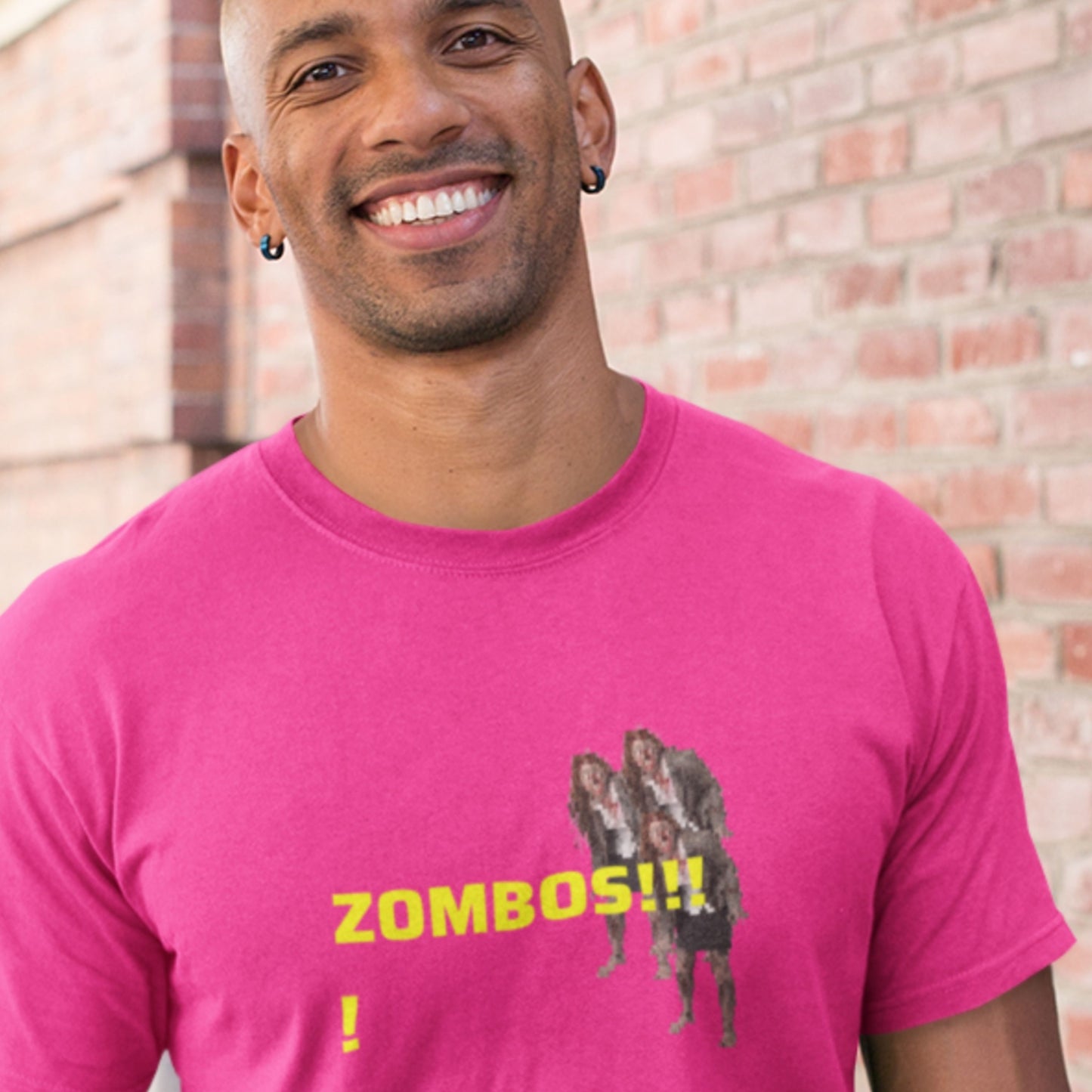 Man wearing a pink t-shirt with 'Zombos!!!' text and graphic design against a brick wall..